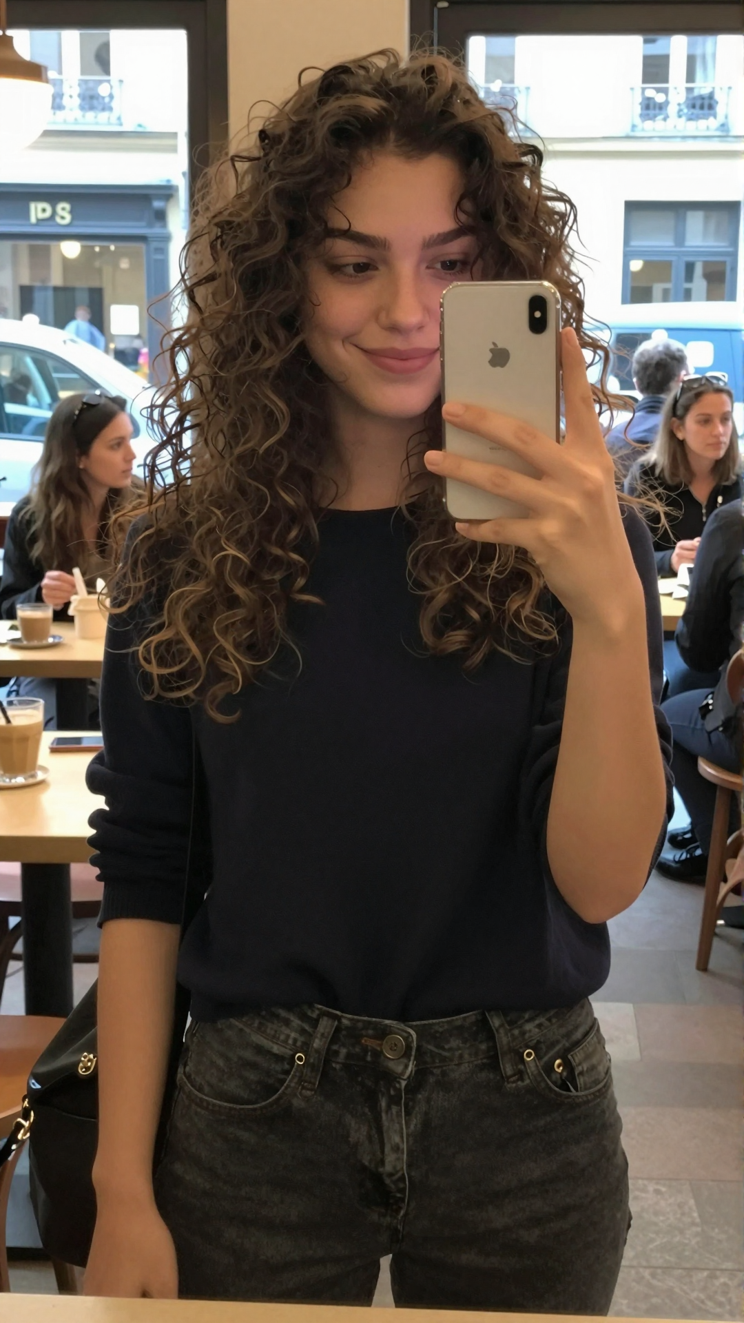 Curly-haired woman taking a mirror selfie inside a café.